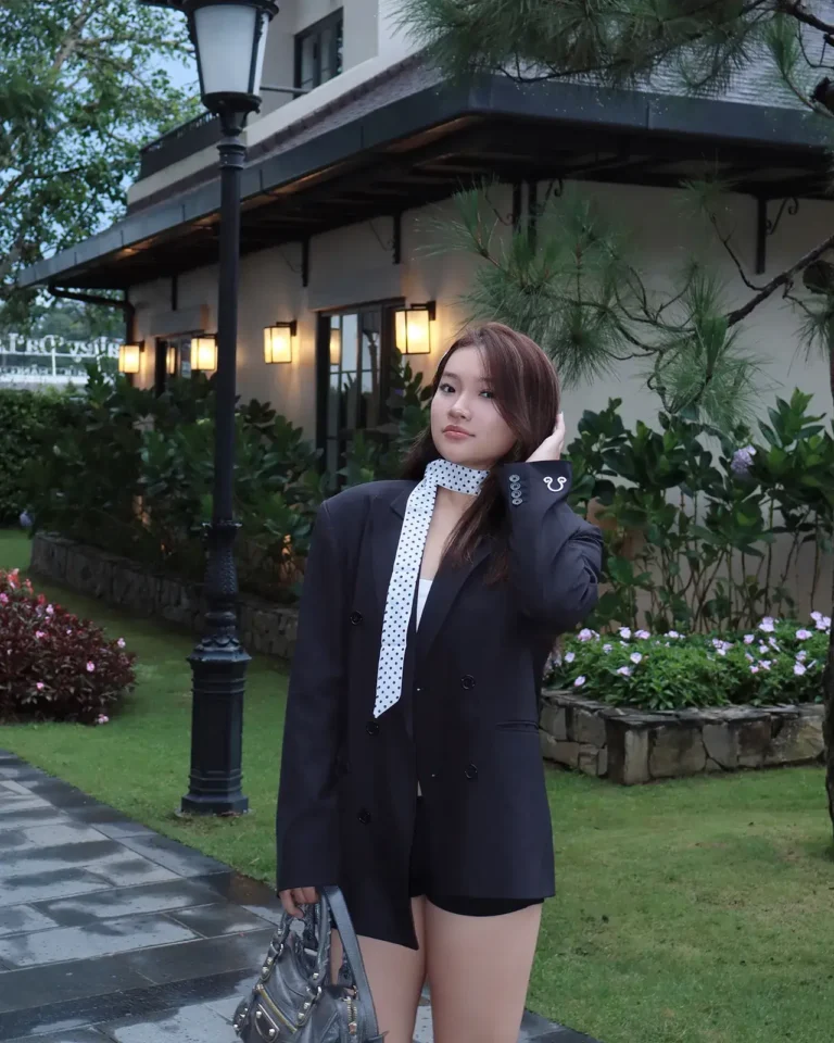 Cô gái mặc blazer đen đứng trong khu vườn cạnh lối đi