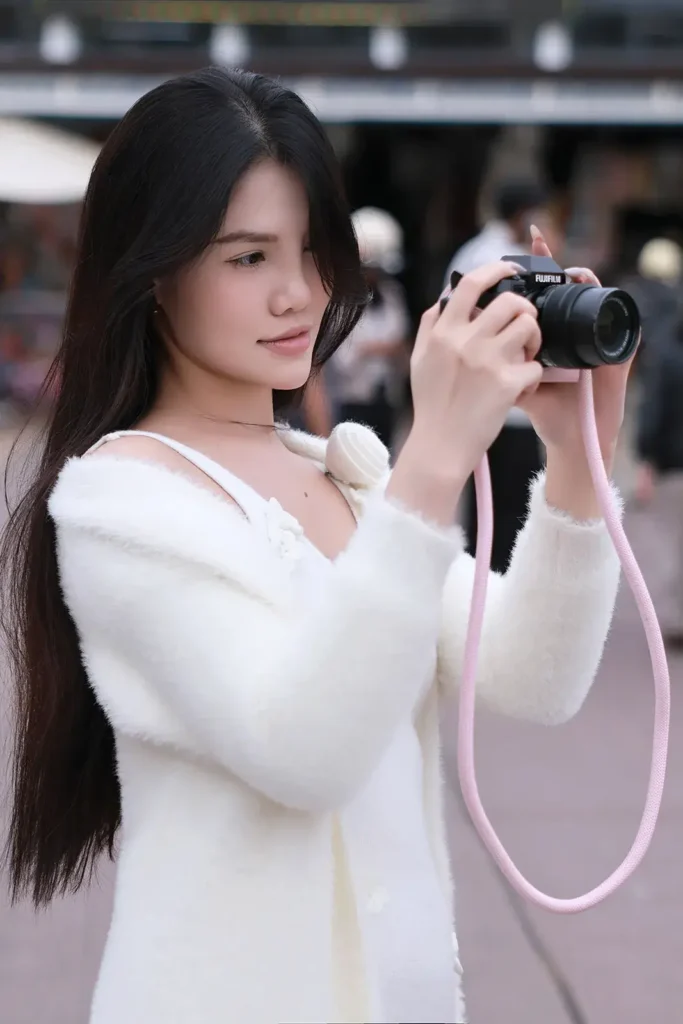 Cô gái mặc áo len trắng cầm máy ảnh Fujifilm dây đeo hồng ngắm chụp trên phố Đà Lạt, ảnh chụp bằng Canon R50