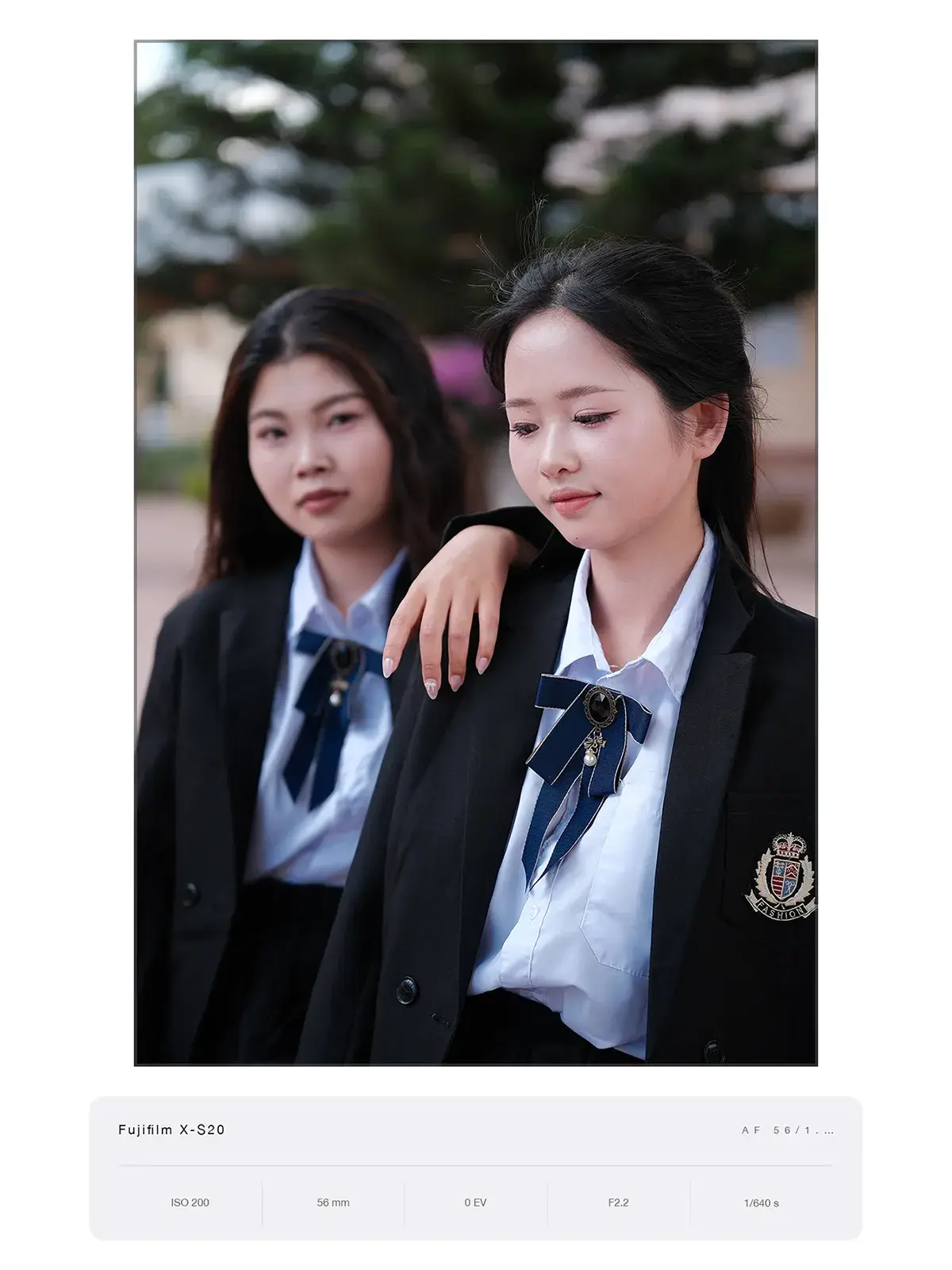 Hai bạn nữ mặc đồng phục vest đen thắt nơ, hậu cảnh xoá phông mềm, chụp bằng Fujifilm X-S20