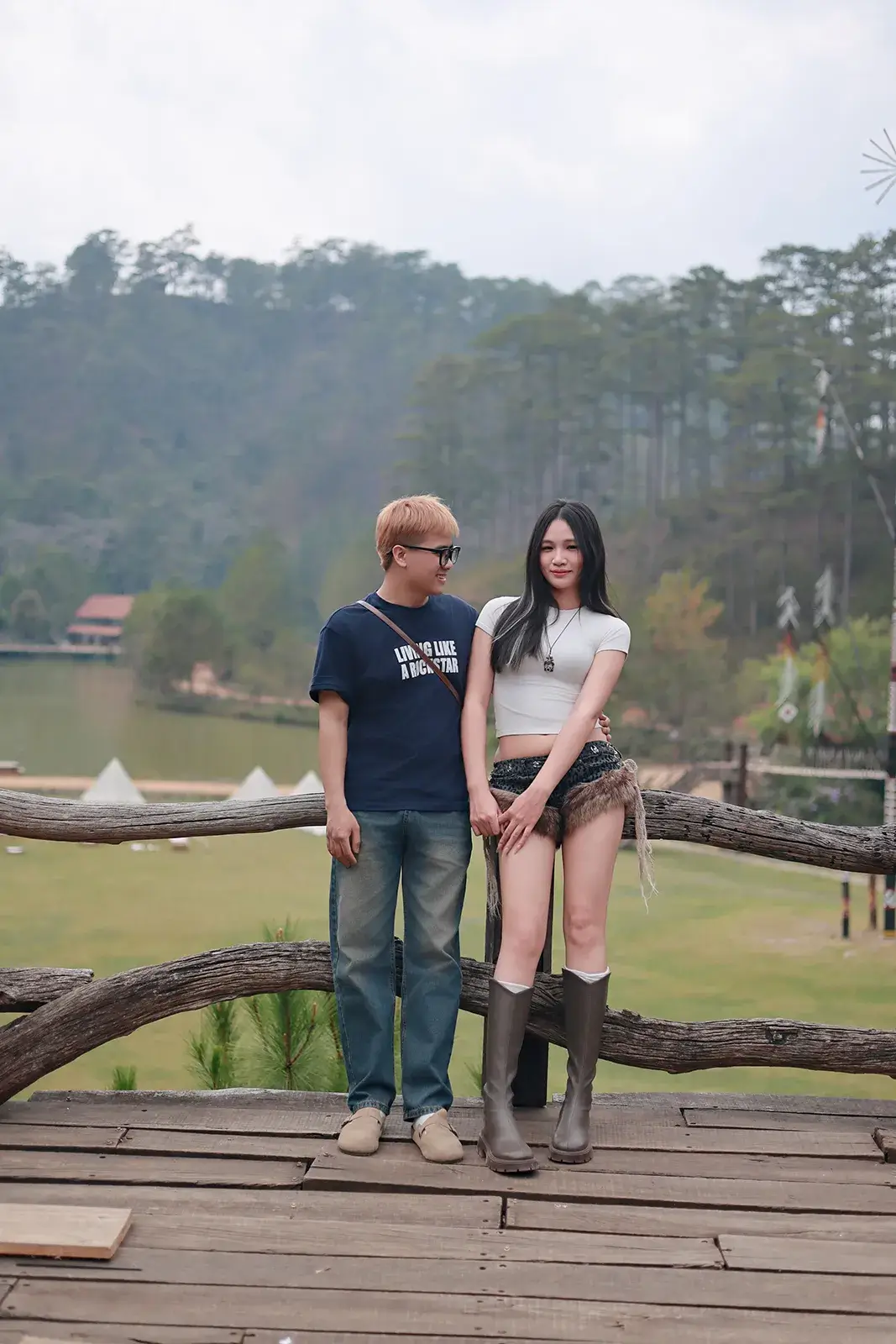 Ảnh couple nắm tay trên sàn gỗ nhìn ra hồ và đồi thông