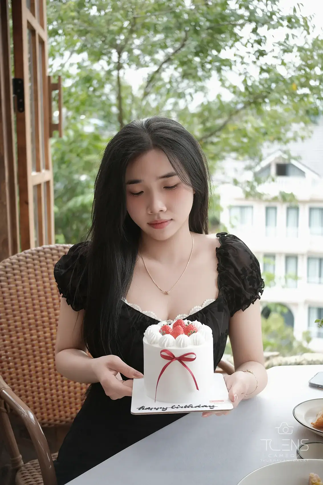 Một phụ nữ mặc váy đen cầm bánh sinh nhật bên cửa sổ, chụp bằng Fujifilm X-T30 với lens 27mm