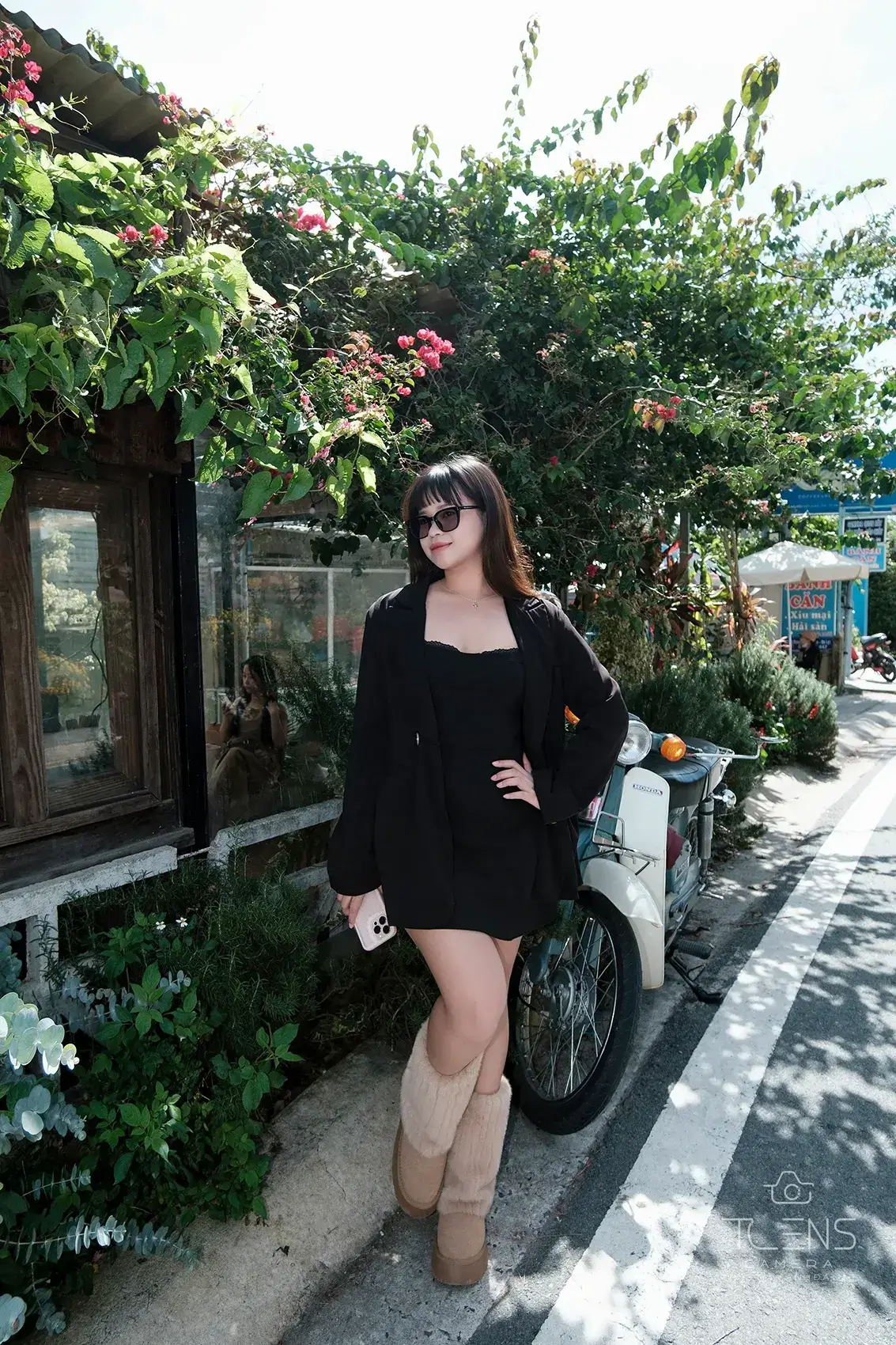 Một phụ nữ mặc đồ đen đứng trên lối đi lát đá giữa cây xanh, chụp bằng Fujifilm X-T30 với XC 15–45mm