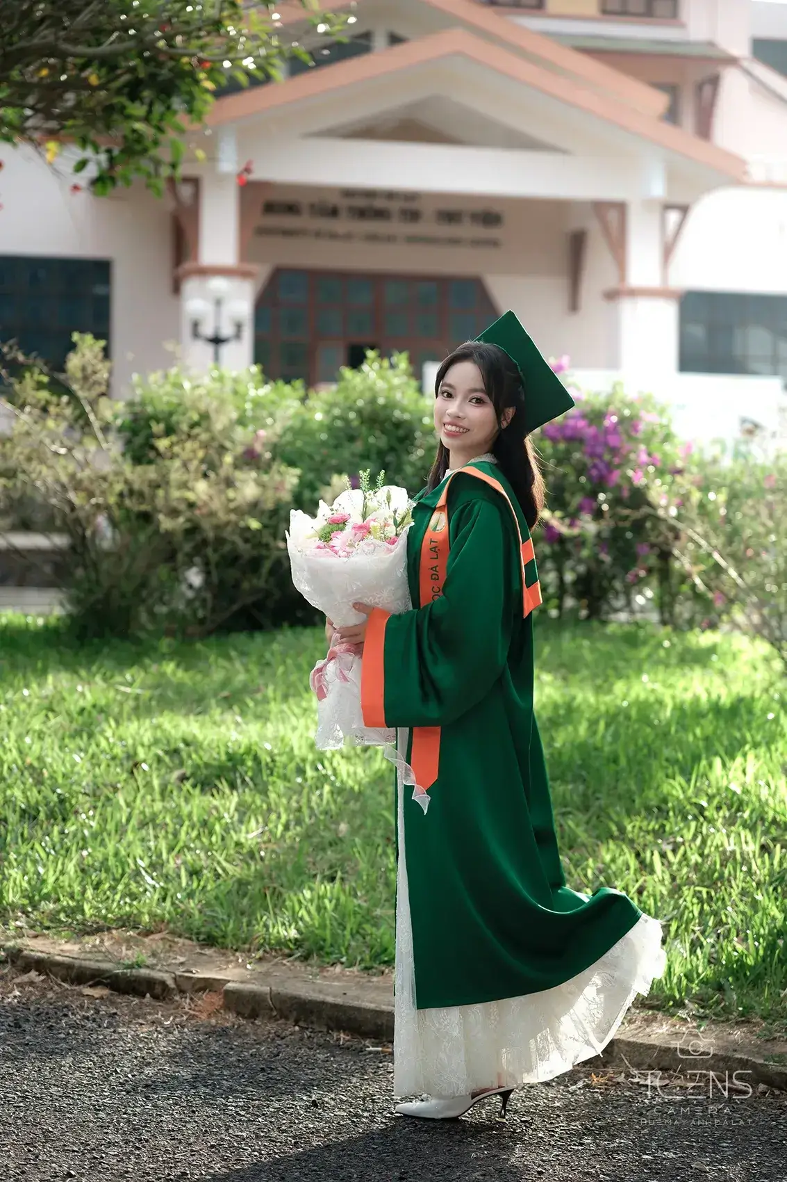 Một phụ nữ mặc áo dài xanh cầm hoa đứng trên bãi cỏ, chụp bằng Fujifilm X-T30 với Viltrox 56mm F1.7