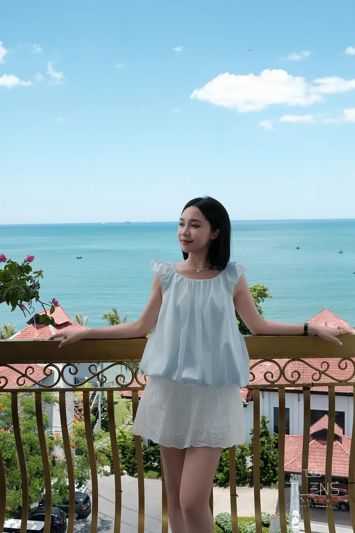 Một phụ nữ mặc váy trắng đứng trên ban công nhìn ra biển, chụp bằng Fujifilm X-T30 và XF23mm F2